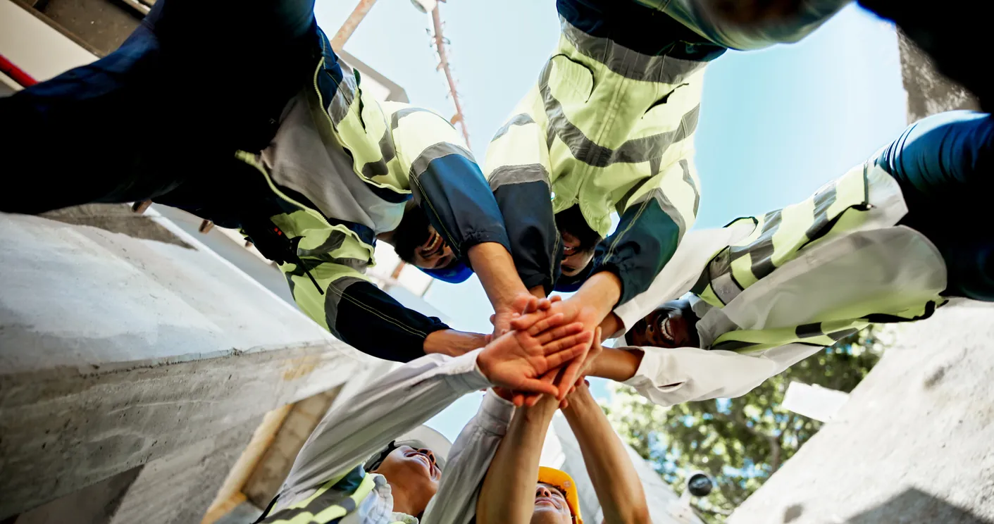 Field crew in high-visibility gear joining hands above a work site