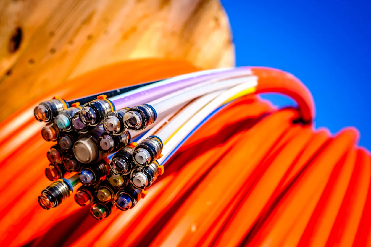 Fibre optic strands and connectors fanned out from an orange cable spool against a clear sky