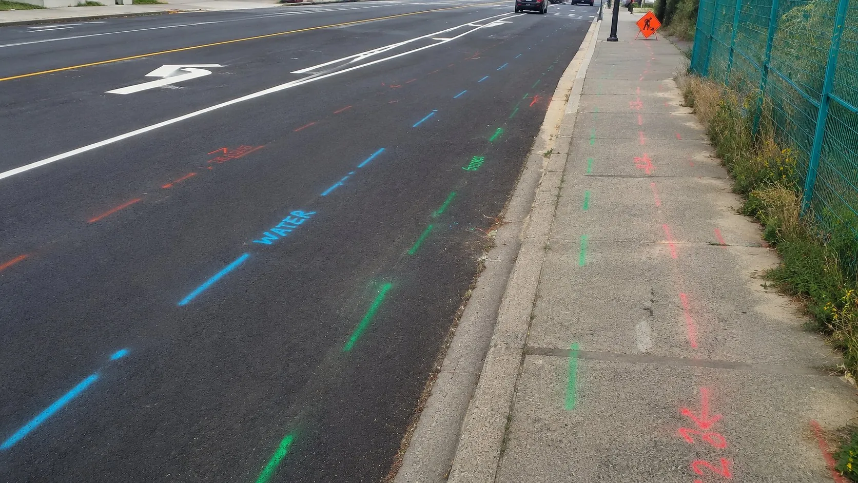 Colour-coded locate marks for water, sewer, and communications running along a municipal roadway and sidewalk